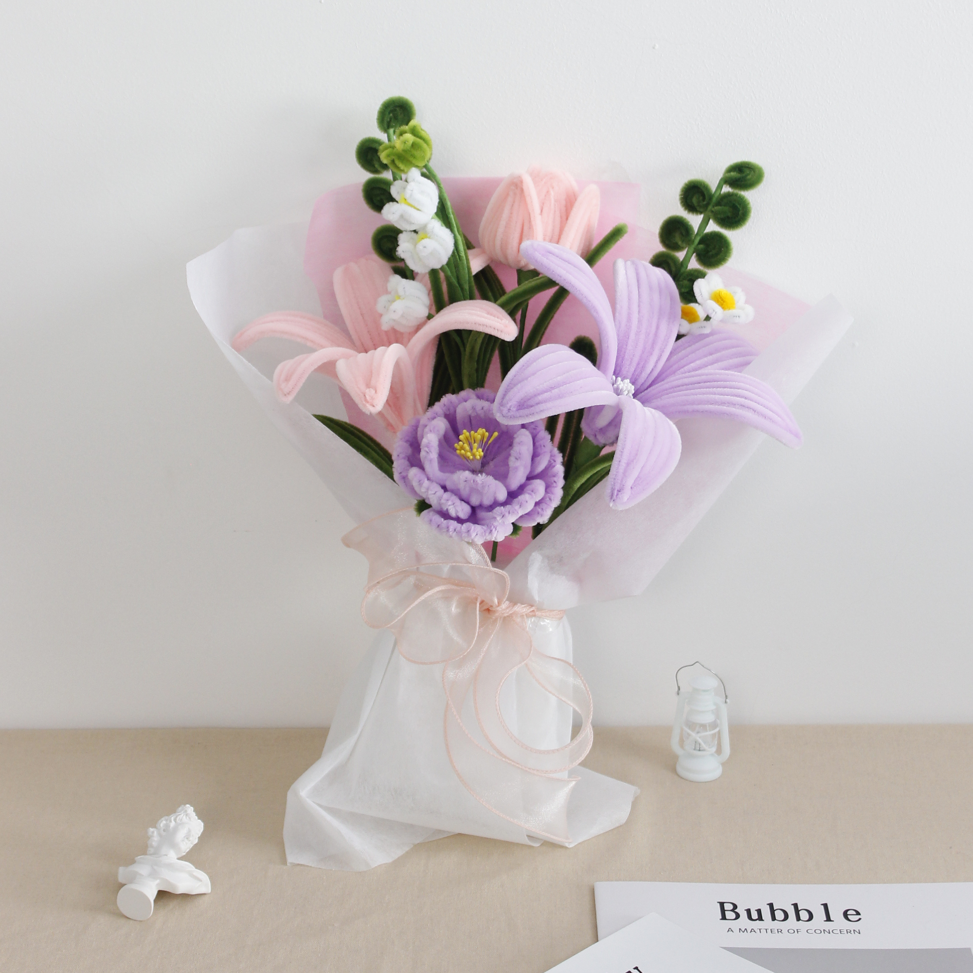 Lily Whisper DIY bouquet made from soft pipe cleaners, featuring pastel lilies, tulips, and a blooming purple carnation. Wrapped in sheer white and pink layers with a soft organza bow a handmade floral gift full of grace.